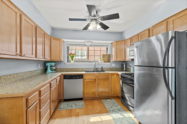 kitchen featuring stainless steel appliances, a sink, light wood finished floors, a ceiling fan, and light countertops