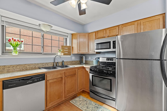 kitchen with stainless steel appliances, a sink, light wood-style flooring, and light countertops
