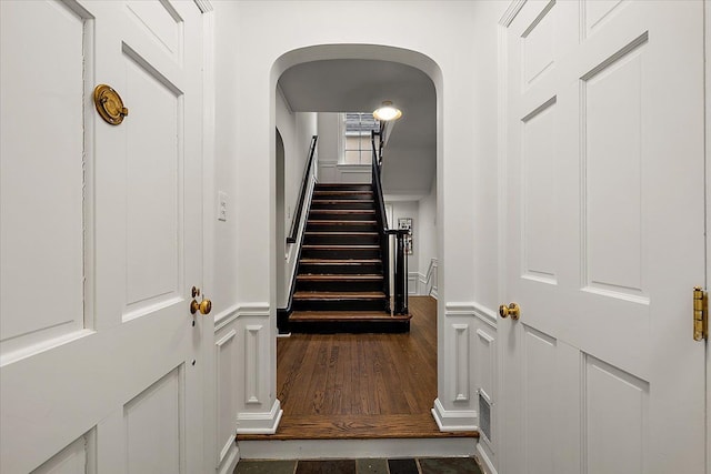staircase featuring arched walkways and wood finished floors