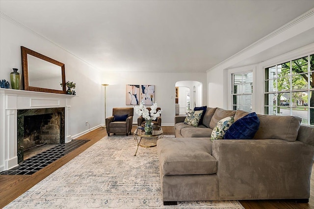 living area with arched walkways, wood finished floors, ornamental molding, a fireplace, and baseboards