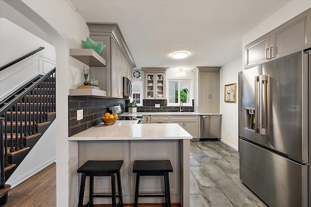kitchen featuring stainless steel appliances, open shelves, gray cabinets, and a peninsula