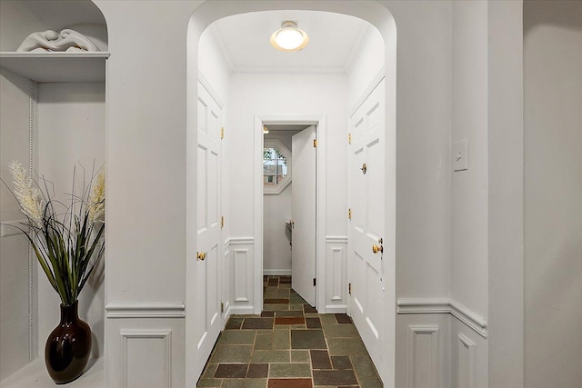 doorway with stone tile floors, crown molding, arched walkways, and baseboards