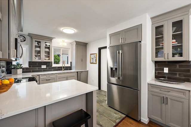 kitchen with appliances with stainless steel finishes, gray cabinets, a sink, decorative backsplash, and glass insert cabinets