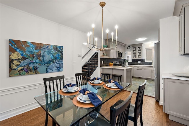 dining space featuring light wood-type flooring, a chandelier, ornamental molding, and stairway