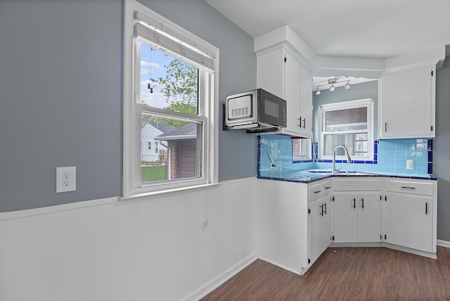 kitchen with a sink, dark wood-style floors, white cabinetry, backsplash, and wainscoting
