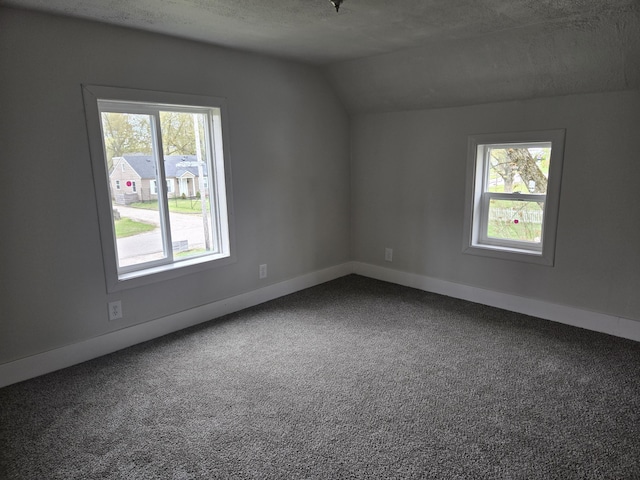 bonus room featuring healthy amount of natural light, lofted ceiling, dark carpet, baseboards, and a textured ceiling