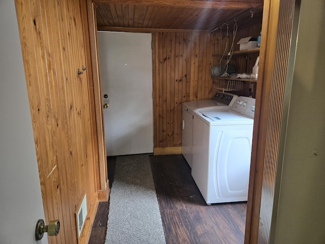laundry room featuring wooden walls, washing machine and clothes dryer, wooden ceiling, and dark wood-style flooring