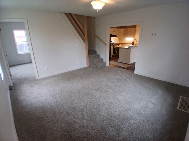 unfurnished living room featuring carpet flooring, stairs, baseboards, and a sink