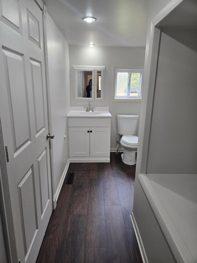 half bath featuring toilet, hardwood / wood-style floors, vanity, and baseboards