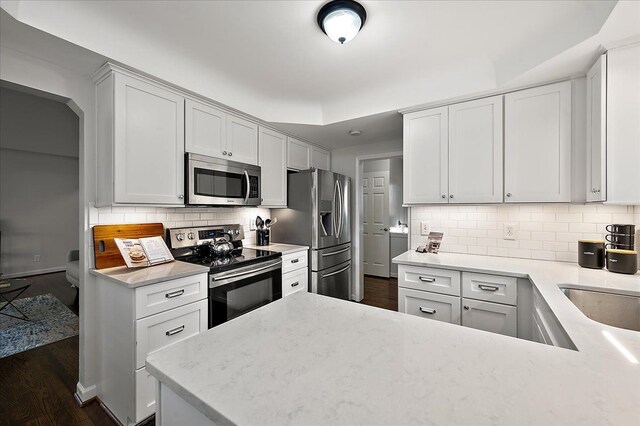 kitchen featuring stainless steel appliances, backsplash, dark wood-style flooring, light stone countertops, and a peninsula