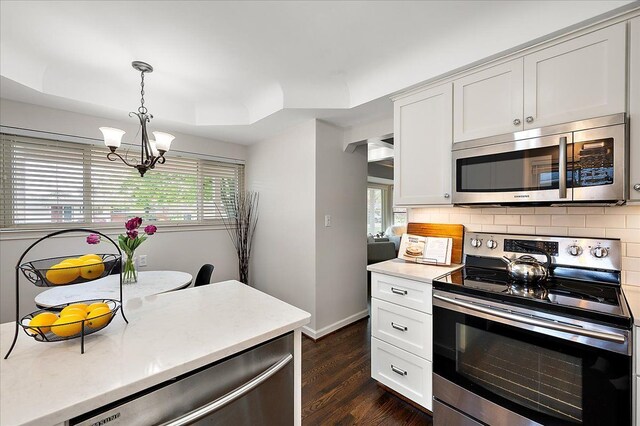 kitchen featuring appliances with stainless steel finishes, a chandelier, dark wood-type flooring, decorative backsplash, and white cabinetry