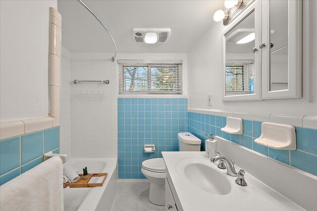 bathroom featuring tile patterned floors, toilet, tile walls, shower / bath combination, and a wainscoted wall