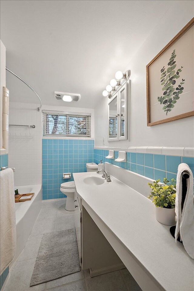 full bathroom featuring vanity, toilet, tile walls, shower / tub combination, and a wainscoted wall