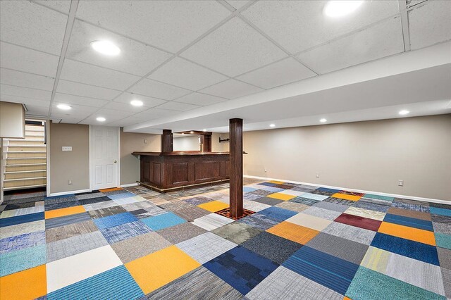 finished below grade area with baseboards, stairway, bar area, recessed lighting, and a paneled ceiling