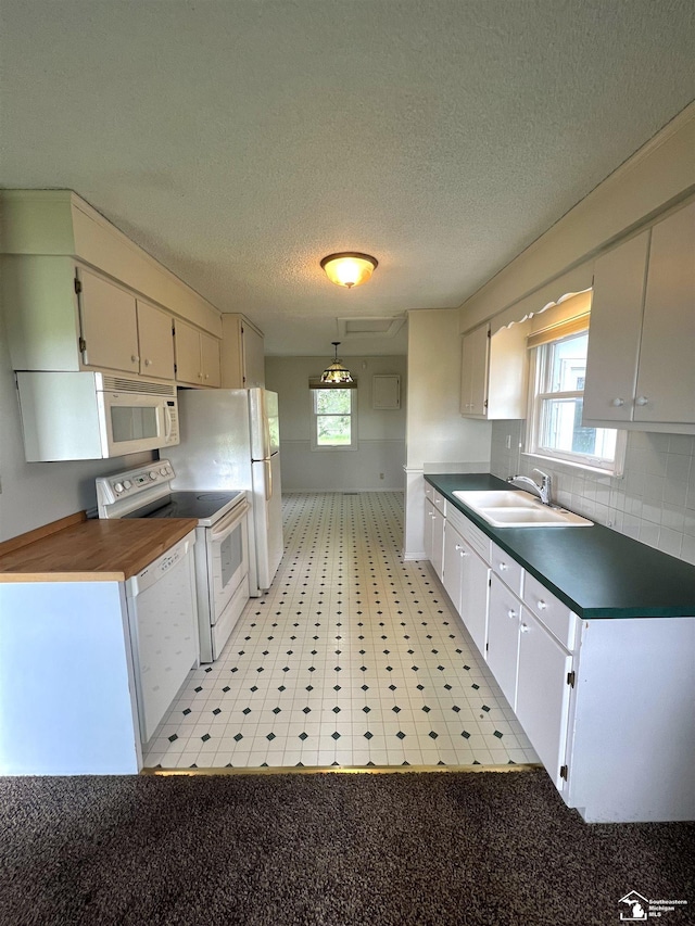 kitchen featuring a sink, white appliances, dark countertops, plenty of natural light, and a textured ceiling