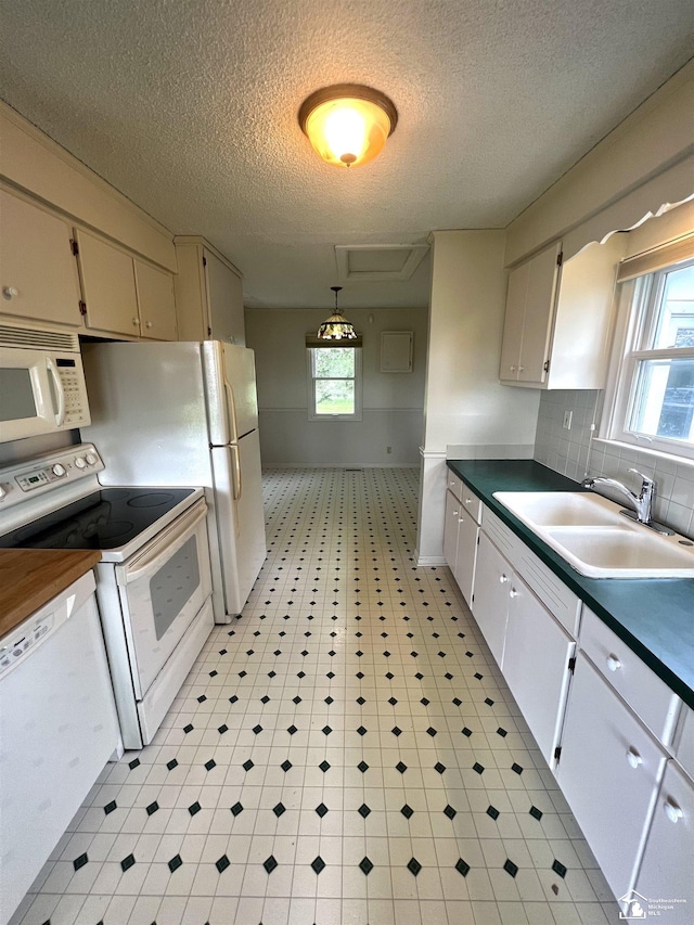 kitchen featuring white appliances, a sink, a textured ceiling, plenty of natural light, and light flooring