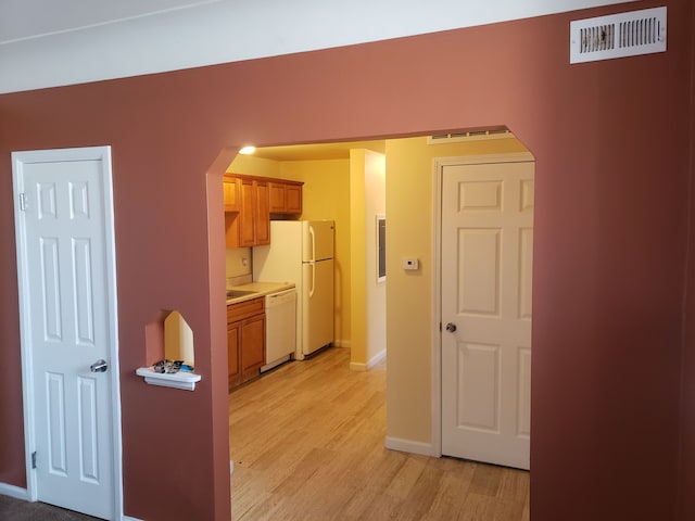 hall with arched walkways, light wood-style floors, and baseboards