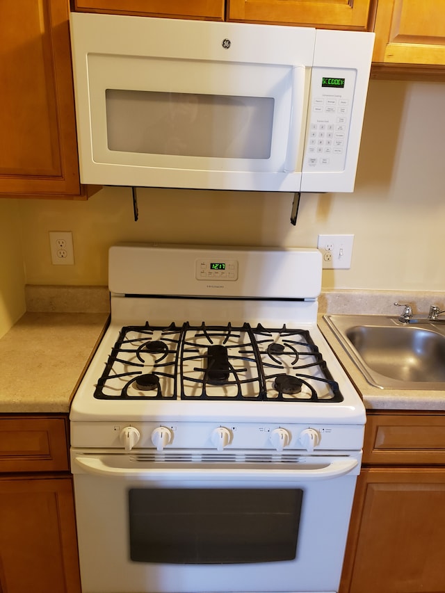 kitchen with white appliances, a sink, light countertops, and brown cabinetry
