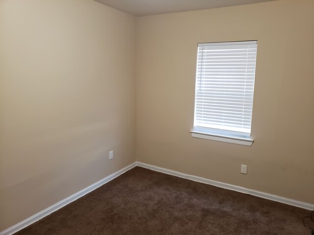 unfurnished room featuring dark carpet and baseboards