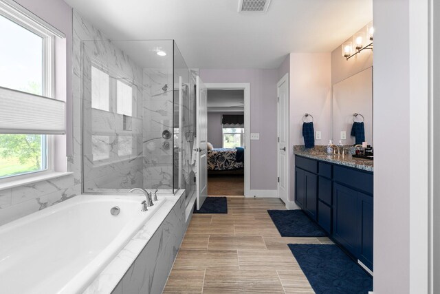 ensuite bathroom featuring healthy amount of natural light, a marble finish shower, vanity, and a bath