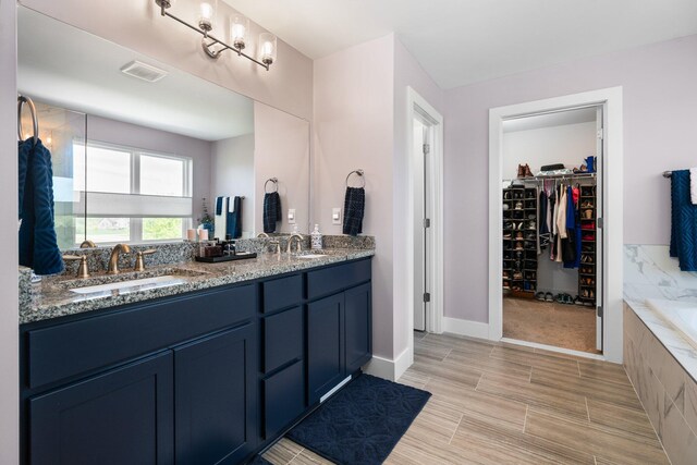 full bathroom with a spacious closet, double vanity, baseboards, a bathtub, and wood finished floors