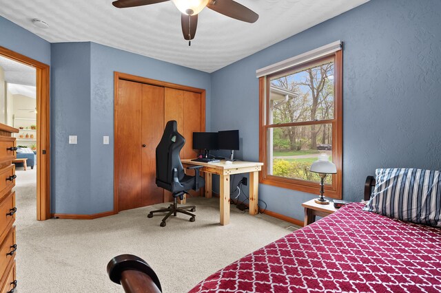 carpeted bedroom featuring baseboards, an office area, a closet, ceiling fan, and a textured wall