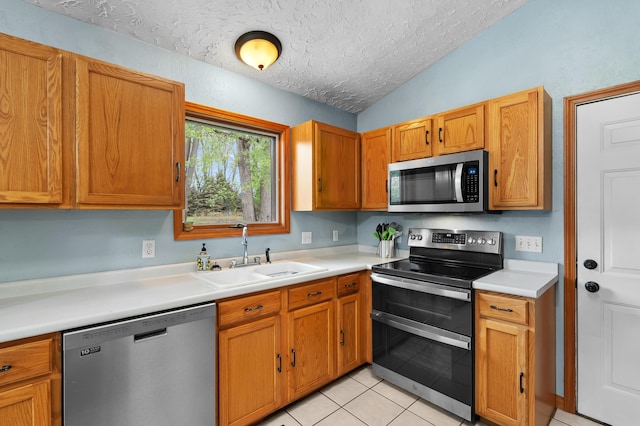 kitchen featuring stainless steel appliances, a sink, a textured ceiling, vaulted ceiling, and light countertops