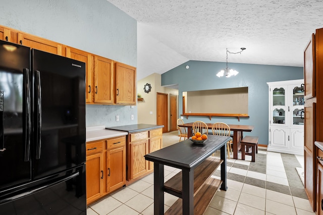 kitchen with freestanding refrigerator, vaulted ceiling, a chandelier, brown cabinets, and decorative light fixtures