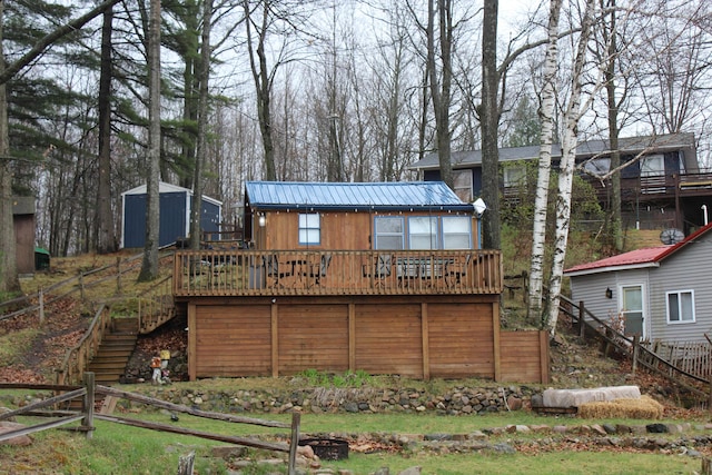 back of property with stairway, a wooden deck, fence, metal roof, and an outbuilding