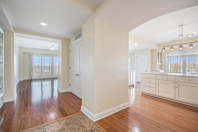 corridor with baseboards, plenty of natural light, arched walkways, wood finished floors, and recessed lighting