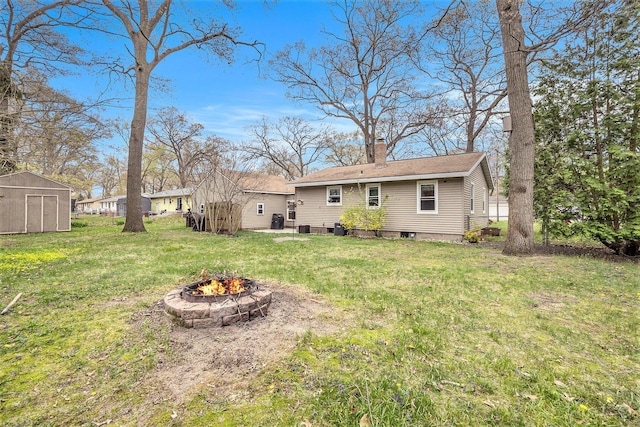 back of house featuring a fire pit, a shed, a chimney, and a yard