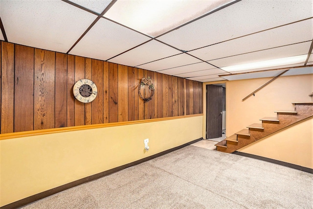 finished basement featuring a drop ceiling, carpet, wood walls, stairway, and baseboards