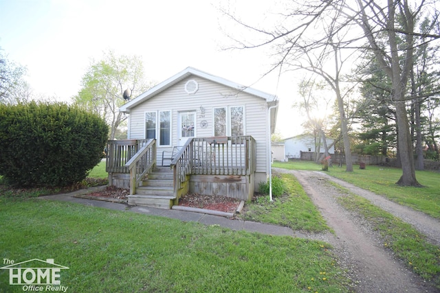 bungalow-style home featuring a front yard, a deck, and dirt driveway