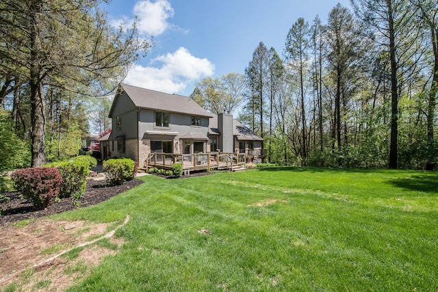 rear view of house featuring a wooden deck, a lawn, a chimney, and a shingled roof