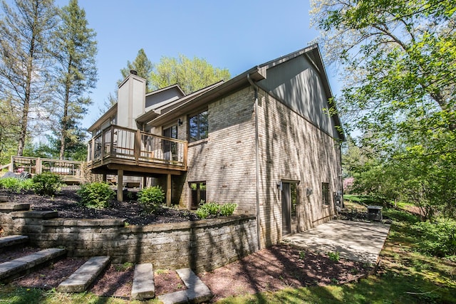 back of house with a chimney, a wooden deck, brick siding, and a patio