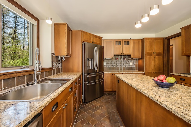 kitchen with stainless steel appliances, a sink, brown cabinets, tasteful backsplash, and decorative light fixtures