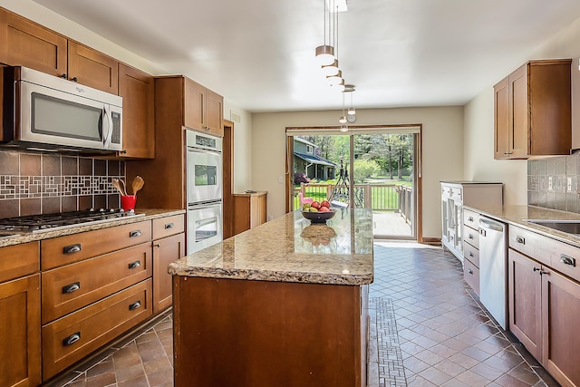 kitchen featuring stainless steel appliances, a kitchen island, brown cabinets, decorative backsplash, and light stone countertops