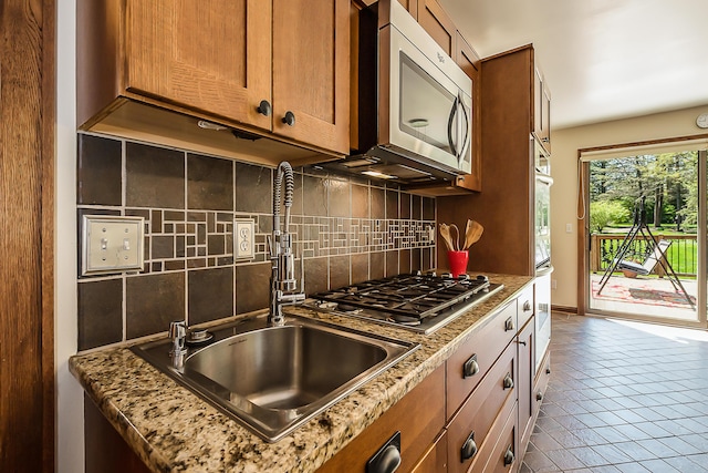 kitchen with stainless steel appliances, backsplash, a sink, and brown cabinets