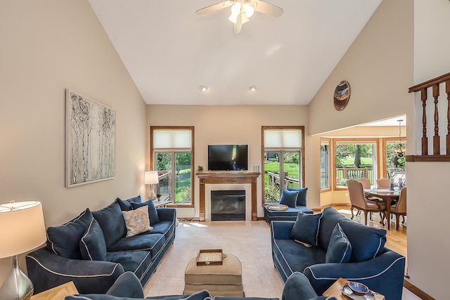 living area with high vaulted ceiling, a glass covered fireplace, ceiling fan, and light colored carpet