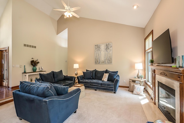 living area with high vaulted ceiling, a fireplace, ceiling fan, baseboards, and light colored carpet