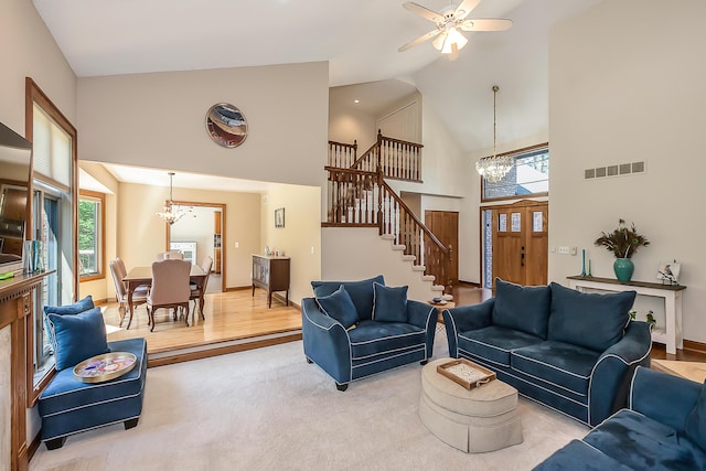 living room featuring a chandelier, high vaulted ceiling, stairway, ceiling fan, and light carpet