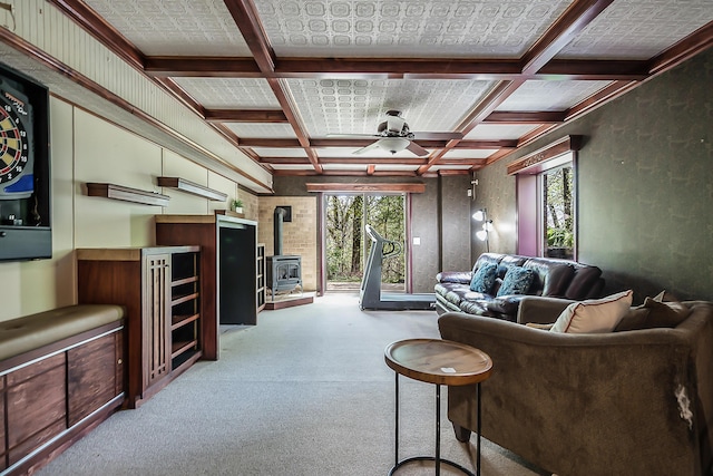 living area with a wood stove, coffered ceiling, ceiling fan, plenty of natural light, and carpet floors