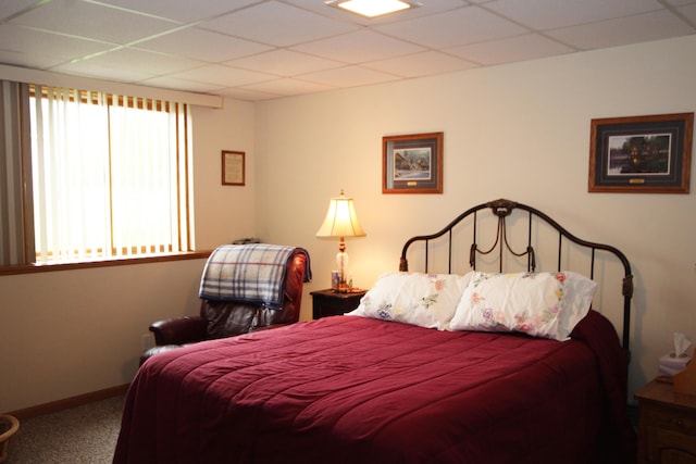 carpeted bedroom featuring a drop ceiling and baseboards
