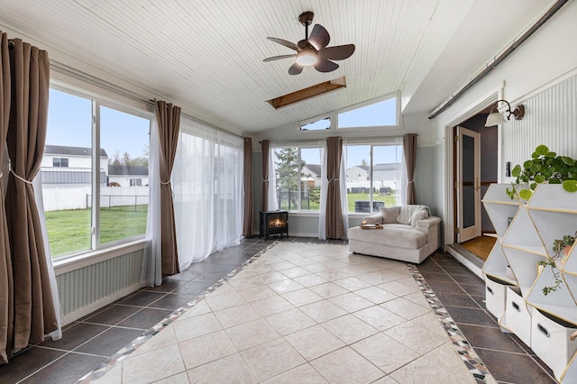 sunroom featuring a wood stove, vaulted ceiling, inlaid floor details, and tile patterned flooring