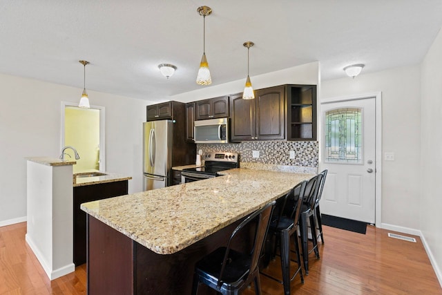 kitchen with stainless steel appliances, a sink, dark brown cabinets, and hardwood / wood-style floors