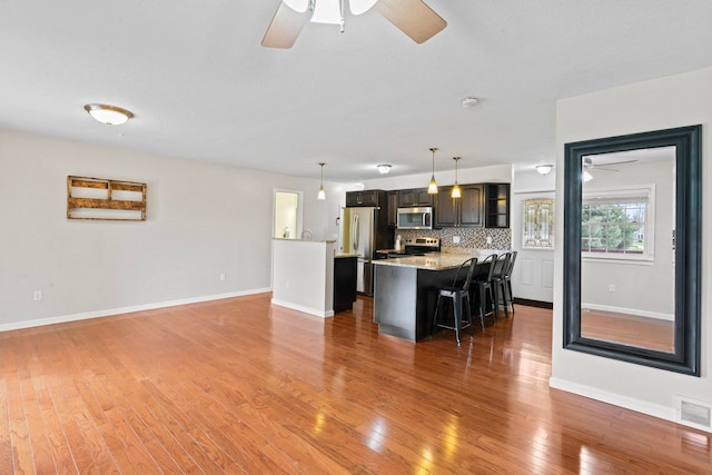 kitchen featuring stainless steel appliances, ceiling fan, a kitchen bar, light wood-type flooring, and hanging light fixtures