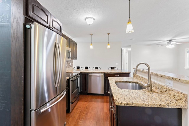 kitchen featuring appliances with stainless steel finishes, a sink, a peninsula, wood finished floors, and a ceiling fan