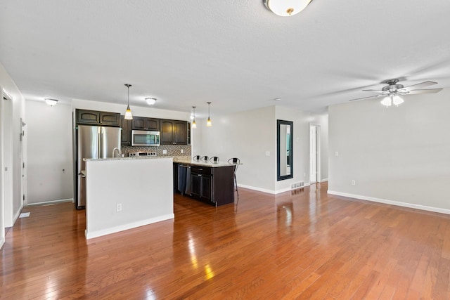 kitchen featuring stainless steel appliances, a kitchen island with sink, light countertops, open floor plan, and decorative backsplash