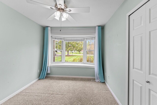 carpeted spare room featuring ceiling fan and baseboards