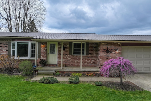 single story home with a garage, metal roof, brick siding, covered porch, and a front lawn